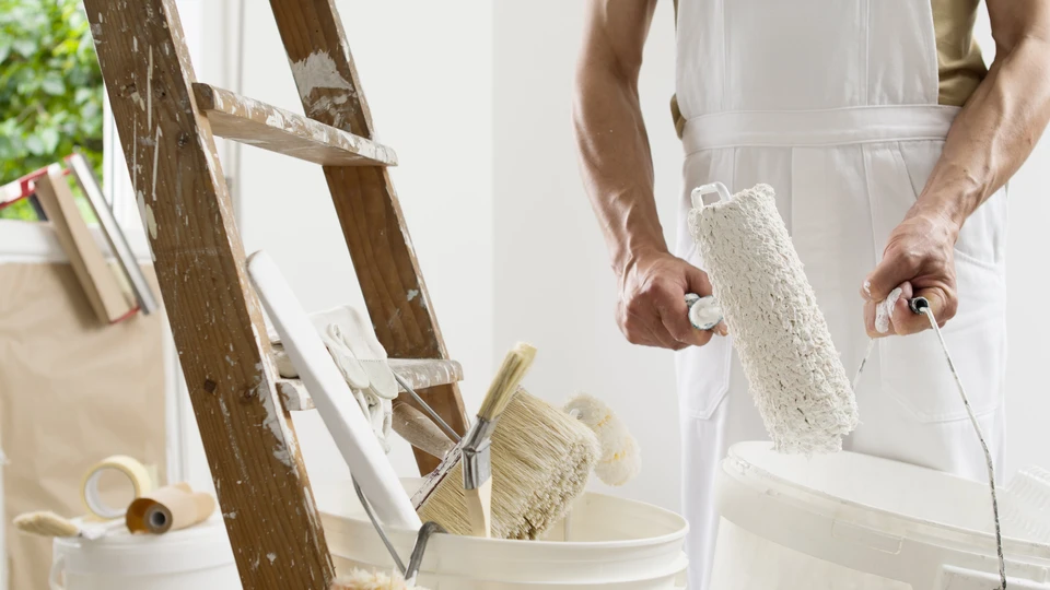 Intérieur résidentiel avec peintre professionnel en salopette blanche tenant un rouleau à poils longs