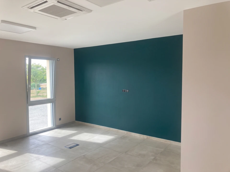 Photographie d'une pièce d'habitation élégante récemment rénovée, montrant des murs fraîchement peints en couleur neutre et apaisante, un plafond impeccable, et un sol en bon état. L'espace doit apparaître lumineux, propre et soigné, incarnant le résultat d'une rénovation intérieure professionnelle. La pièce doit être meublée simplement de manière moderne et accueillante, sans présence d'artisan ni de matériel de chantier.