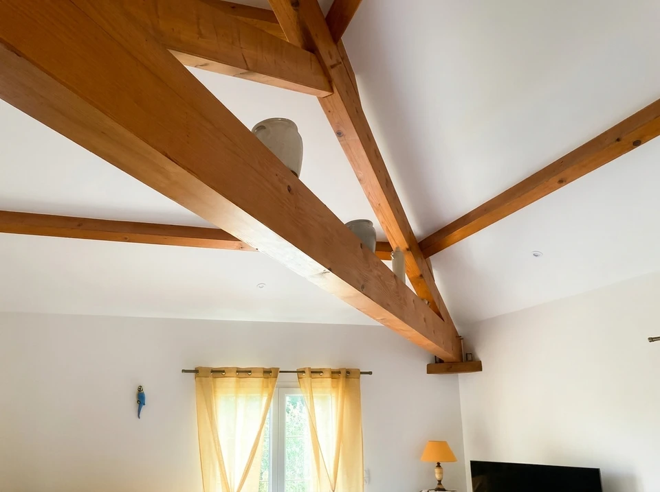 Photographe d'un ouvrier du bâtiment en tenue de travail appliquant de la peinture sur un mur intérieur avec un pinceau, montrant les différentes étapes de travail : à gauche du cadre, des plaques de plâtre partiellement installées, au centre l'ouvrier peignant méthodiquement, et à droite un mur déjà partiellement fini. La scène capture le professionnalisme et la progression du travail de rénovation intérieure, avec outils et matériaux visibles en arrière-plan.